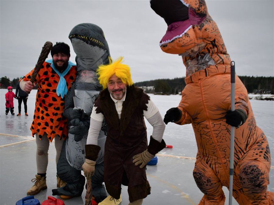 Fire deltakere i dinosaur- og huleboerkostymer på isen med curlingstener